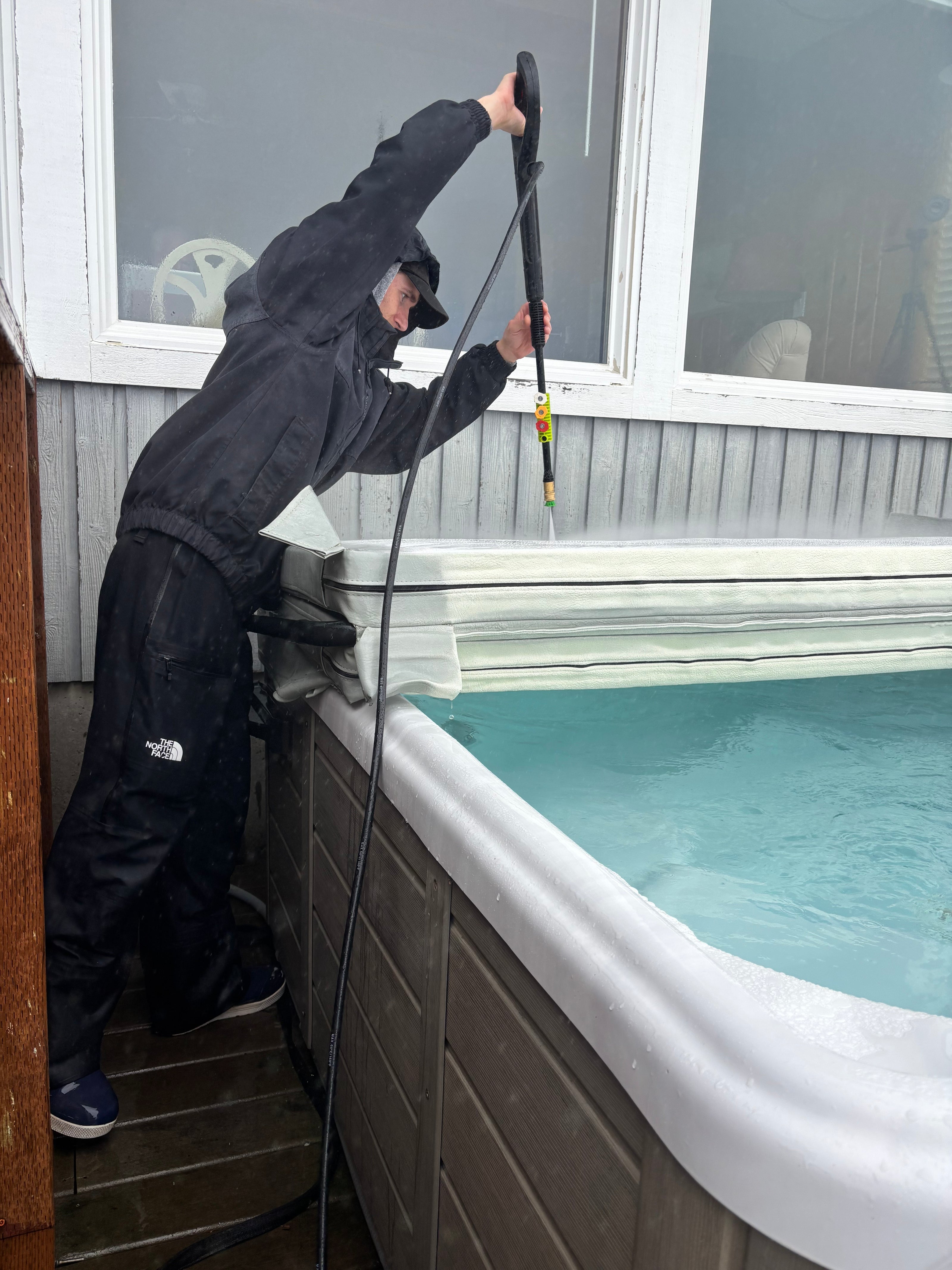 Person cleaning hot tub cover with a powerwasher.